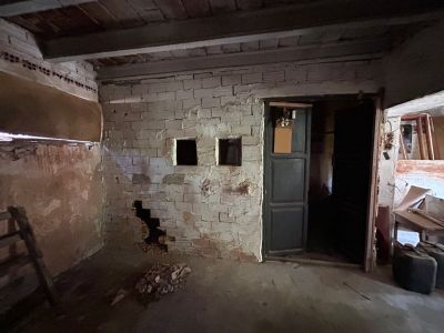 Interior en bruto con paredes de ladrillo visto, techo de vigas de madera y aberturas. Un espacio con potencial para una reforma integral, mostrando su estado actual.