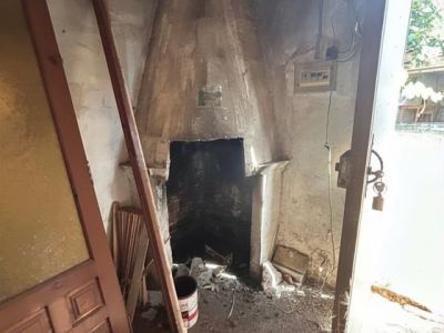 Interior en bruto con una chimenea tradicional de obra, paredes sin revestir y suelo con escombros. Se observa una puerta de madera y luz natural, listo para una reforma integral.