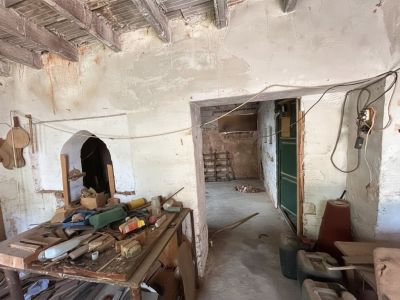 Interior en estado de reforma con vigas de madera expuestas y paredes desconchadas. Destaca un arco decorativo en la pared izquierda y un banco de trabajo desordenado.