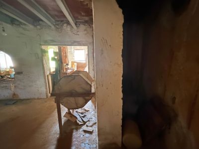 Interior en reforma con vigas de techo expuestas y paredes sin acabar. Una estructura de madera octogonal destaca en el centro, con luz natural al fondo.