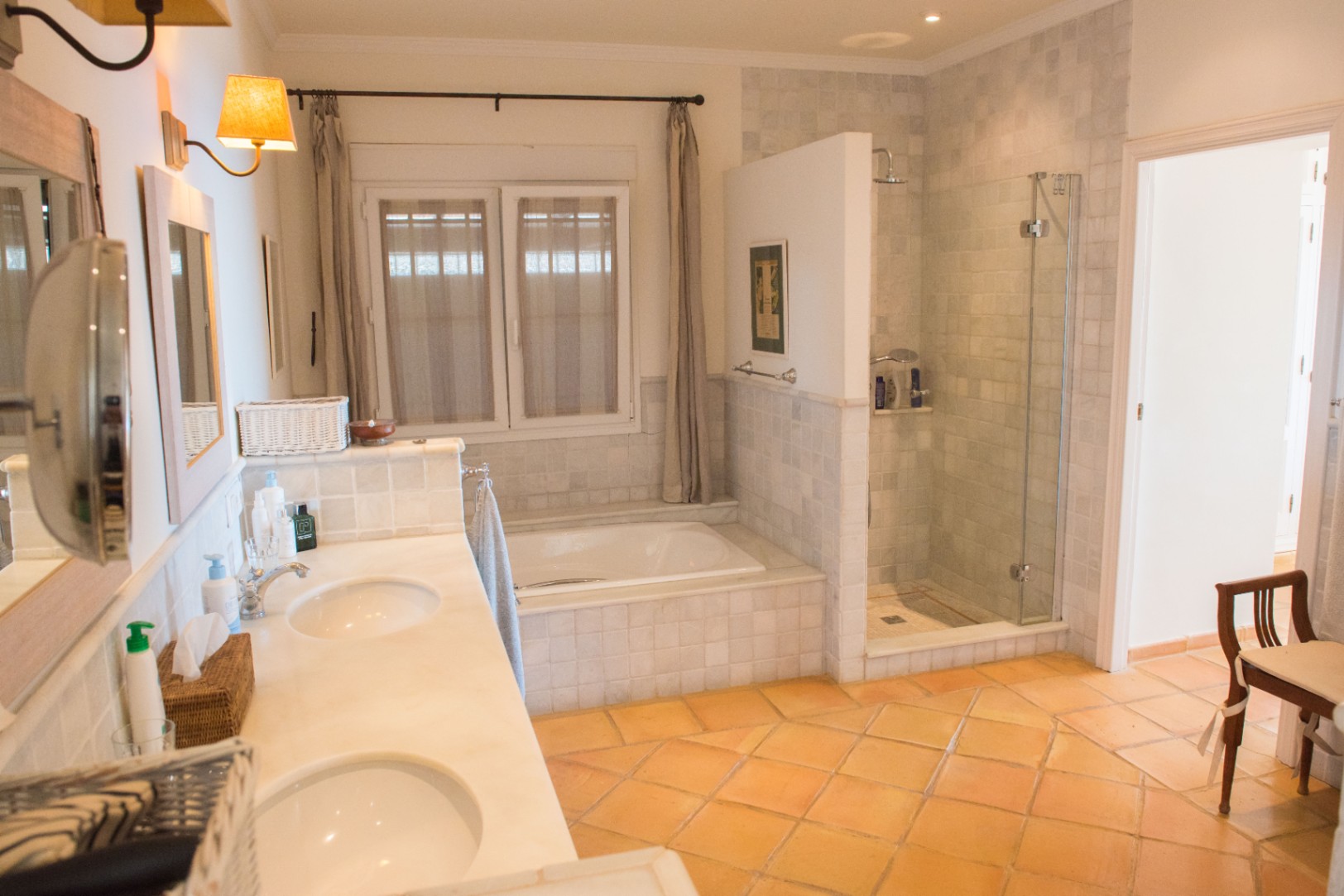 Amplio cuarto de baño con lavabo doble de mármol, suelos de terracota, bañera encastrada y una zona de ducha independiente con mampara de cristal.