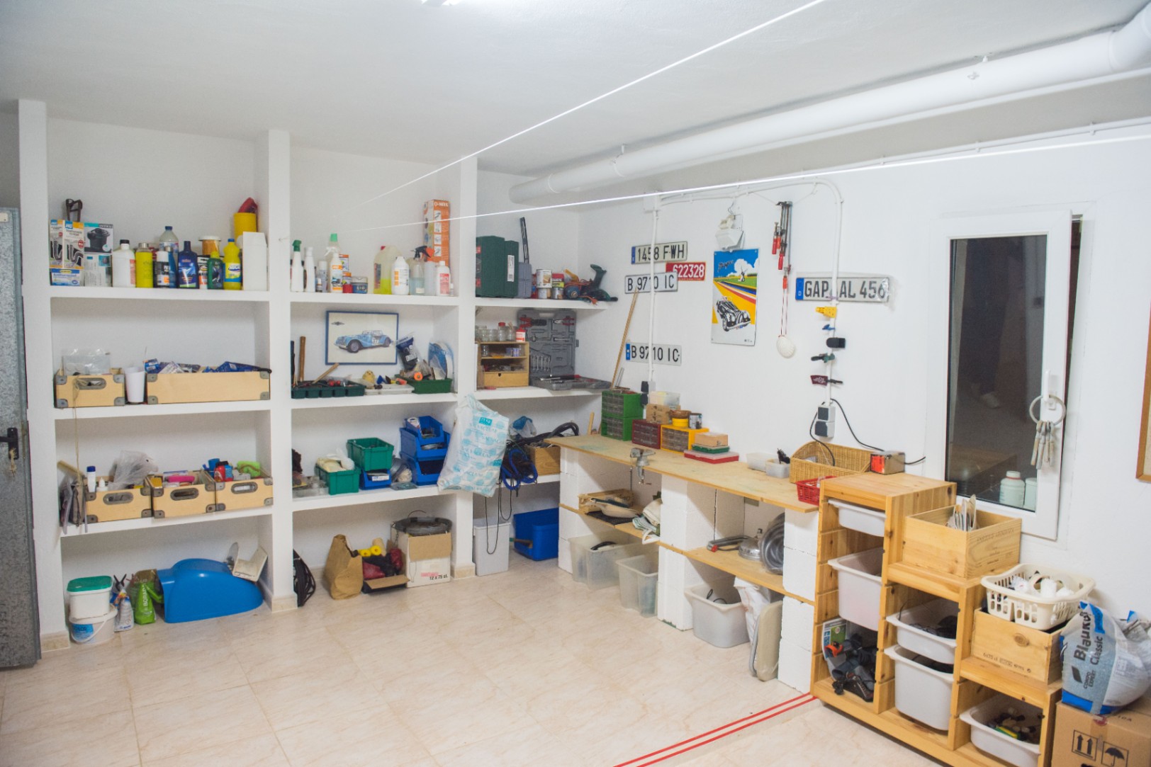 Amplio taller y zona de almacenaje con estanterías de obra, banco de trabajo de madera y suelos cerámicos, ideal para mantenimiento y proyectos.