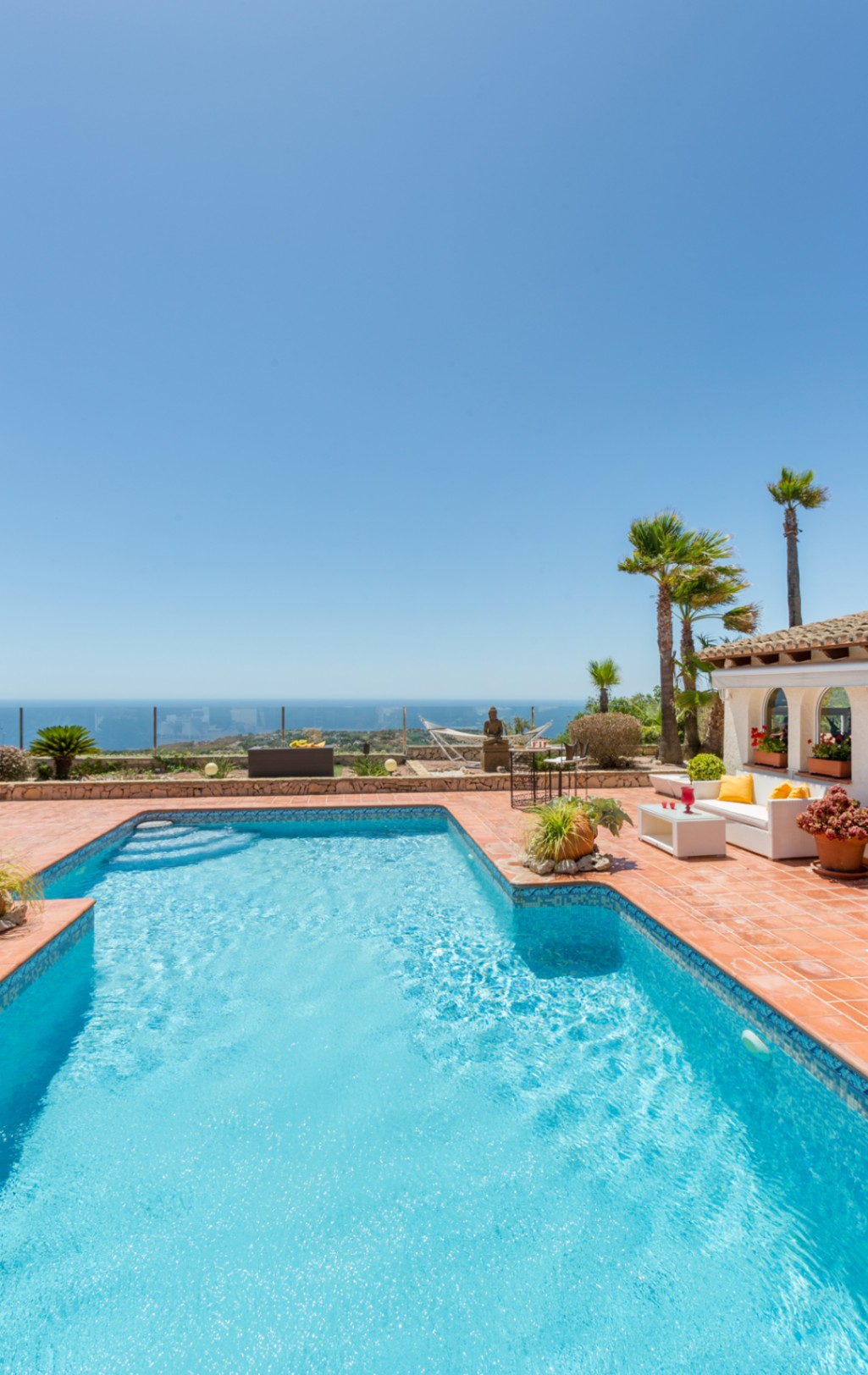 Piscina con mosaico azul y terraza de terracota con zona de estar, palmeras y vistas panorámicas al mar Mediterráneo en Cumbre del Sol.