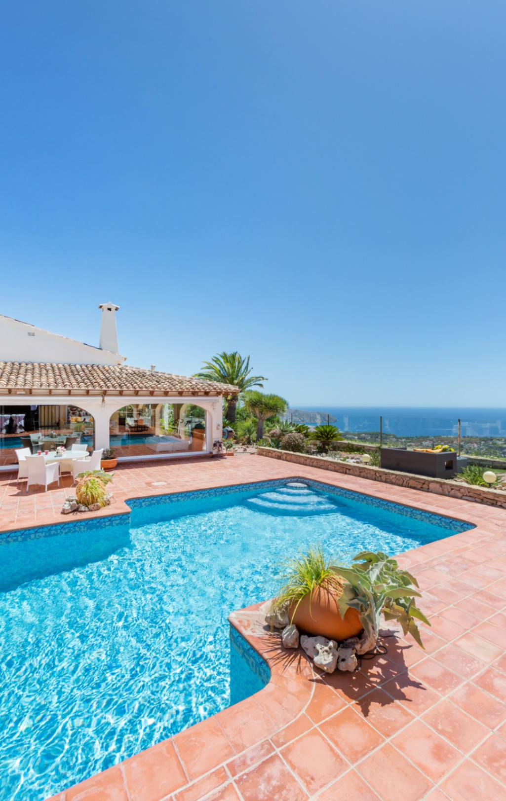 Piscina exterior con mosaico azul y terraza de terracota, con vistas panorámicas al mar Mediterráneo y la costa de Cumbre del Sol.