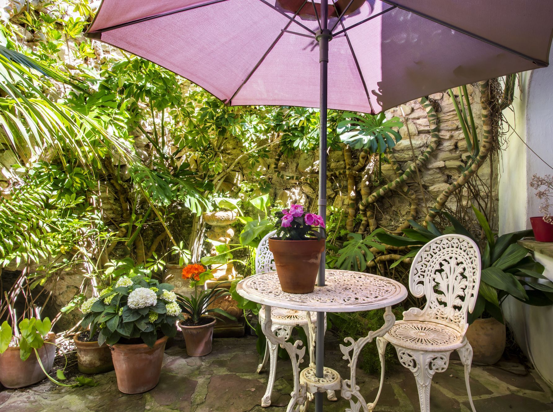 Íntimo patio con mesa de hierro forjado, rodeado de vegetación y muros de piedra.