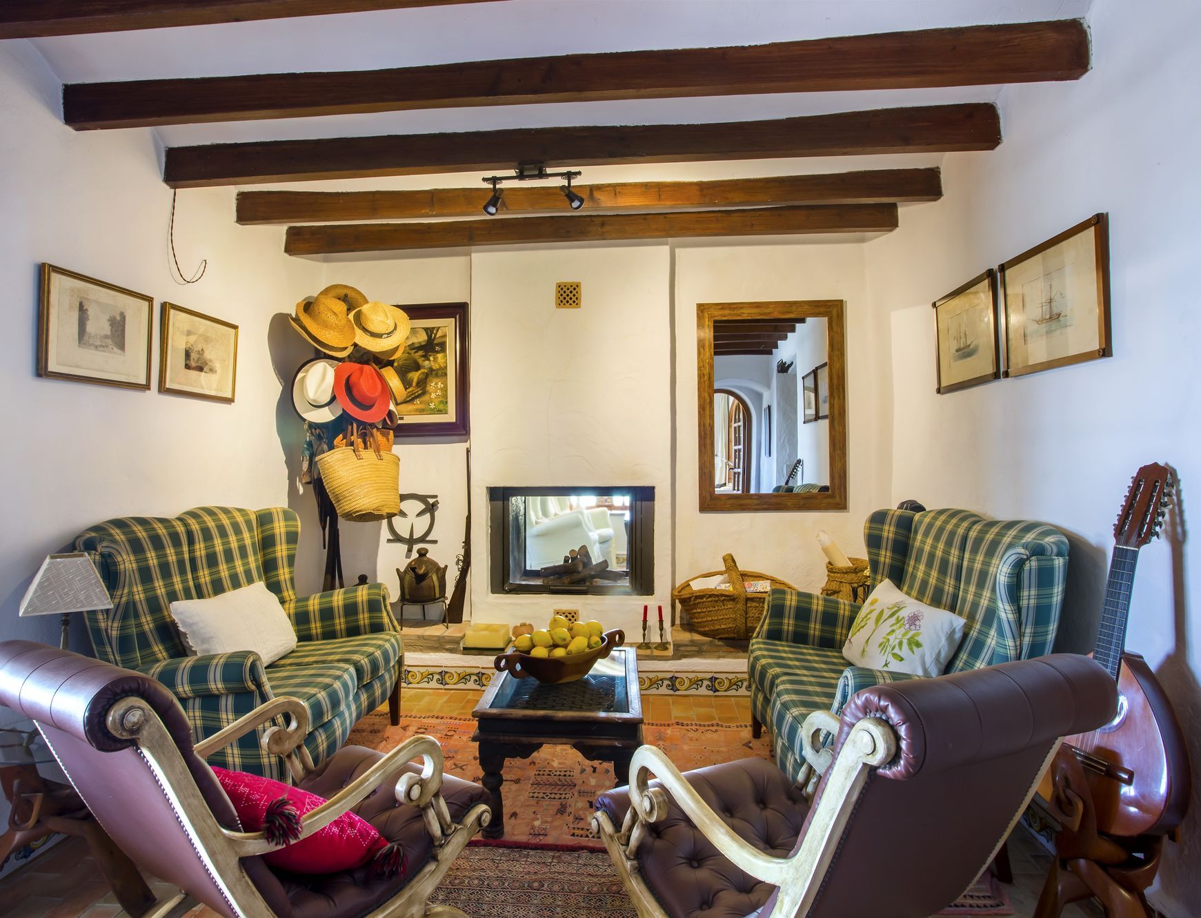 Salón rústico con chimenea, sillones de cuadros y vigas de madera a la vista. Decoración tradicional y luz natural.