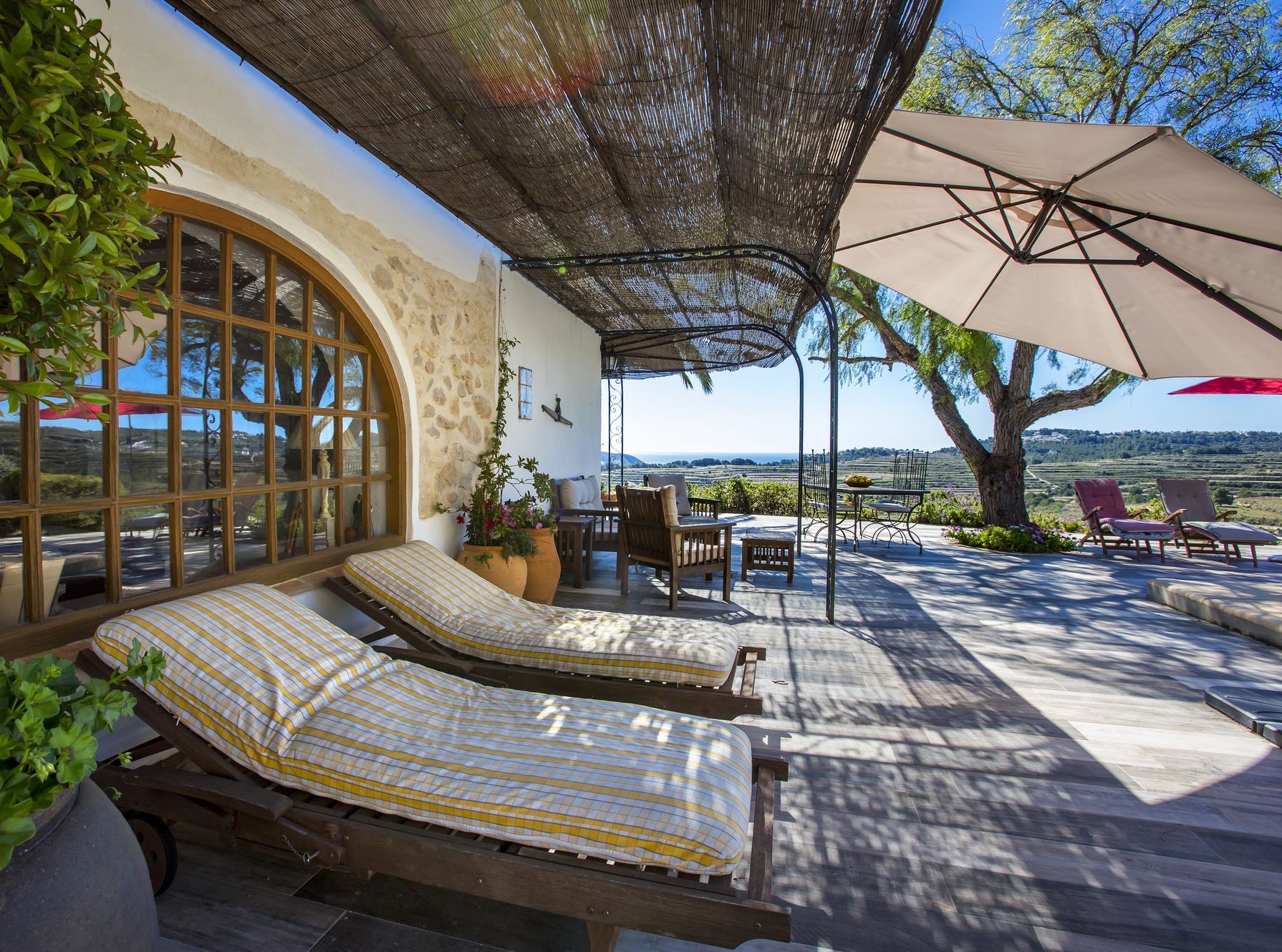 Terraza cubierta con tumbonas de madera y vistas al mar, protegida por un toldo de brezo.
