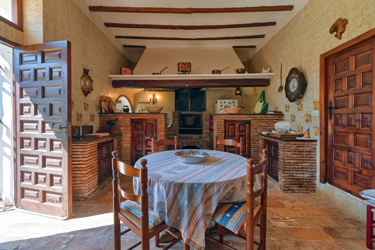 Cocina rústica tradicional con gran hogar de ladrillo visto, vigas de madera en el techo y suelos de terracota originales en un espacio acogedor.