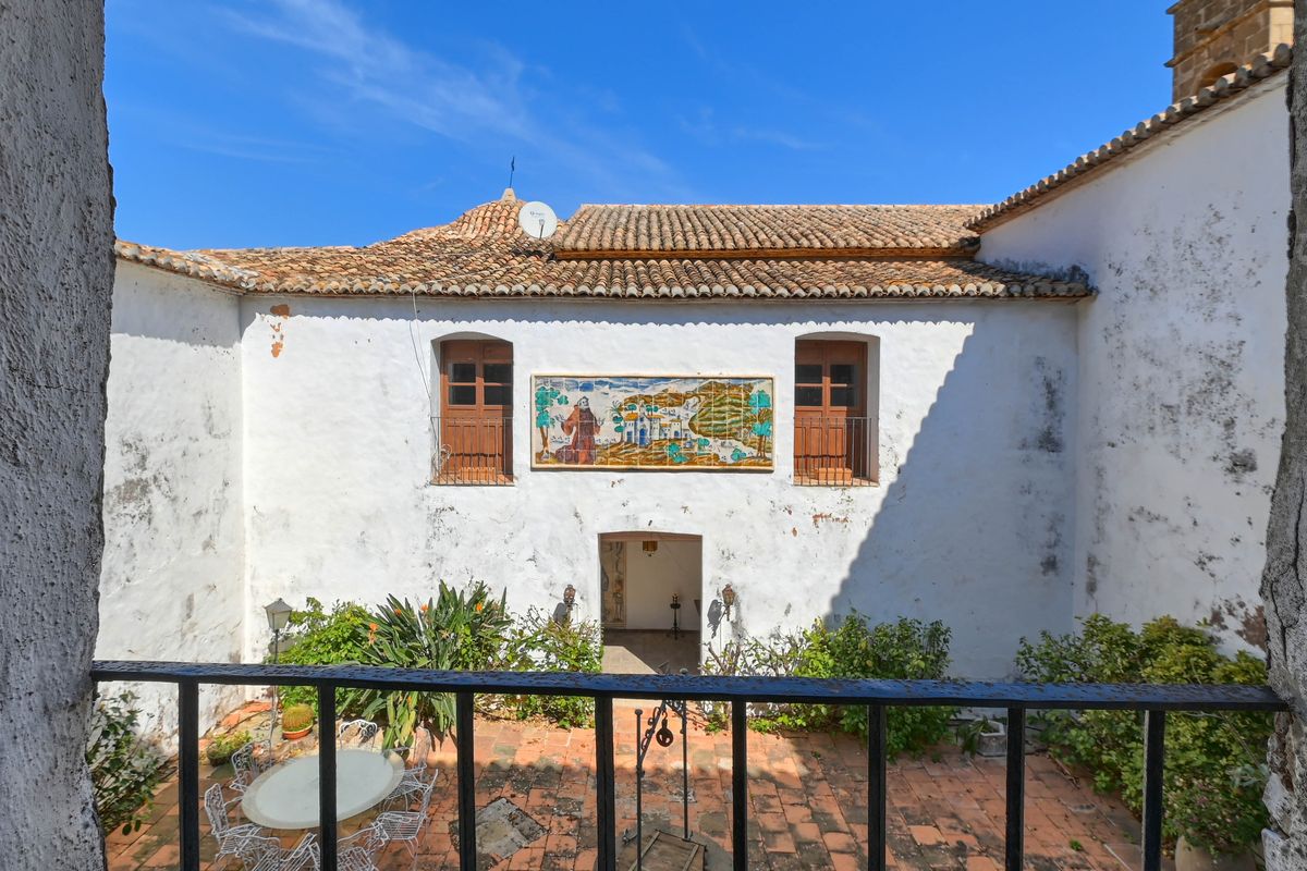 Patio interior tradicional con suelos de terracota, un mural decorativo de azulejos y fachadas de cal blanca bajo un cielo despejado.