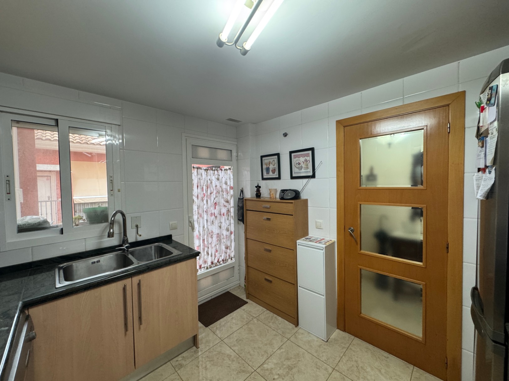 Cocina funcional con encimera de granito negro, baldosas cerámicas y puerta de madera con paneles de vidrio.