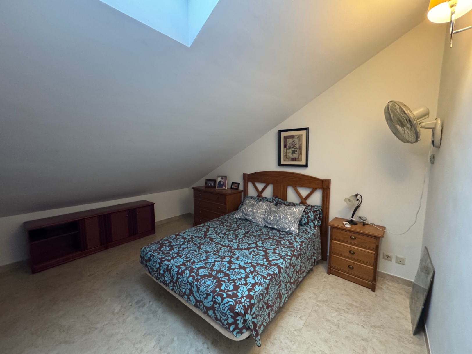 Dormitorio abuhardillado con cama doble, cómoda de madera y tragaluz.