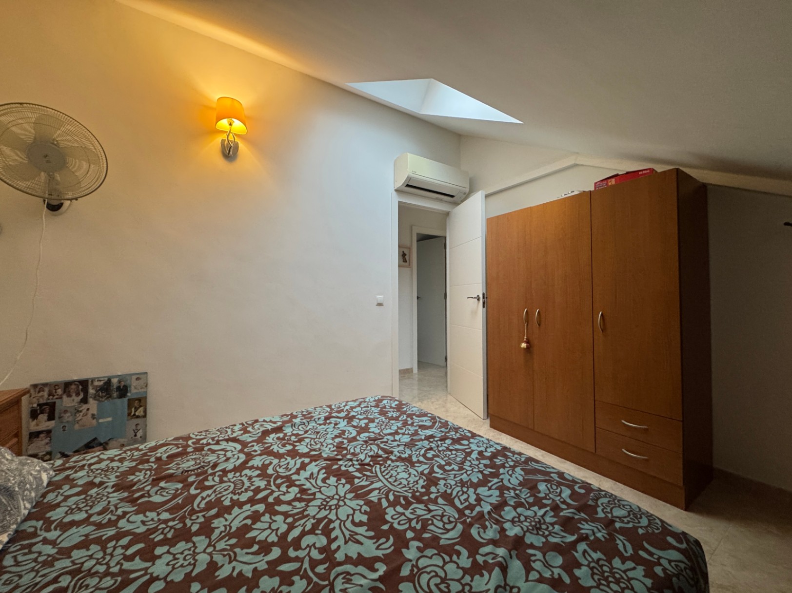 Dormitorio con cama estampada, armario de madera y luz ambiental cálida.