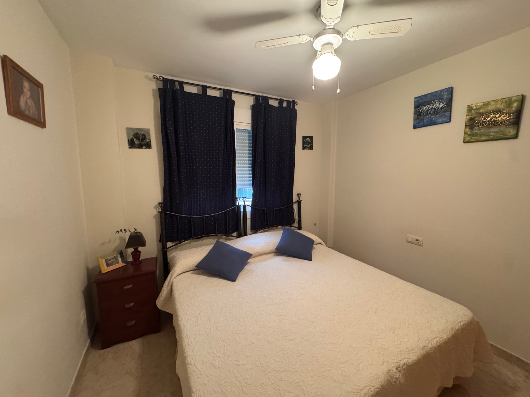 Dormitorio luminoso con cama doble, cortinas azul marino y mesita de noche de madera.