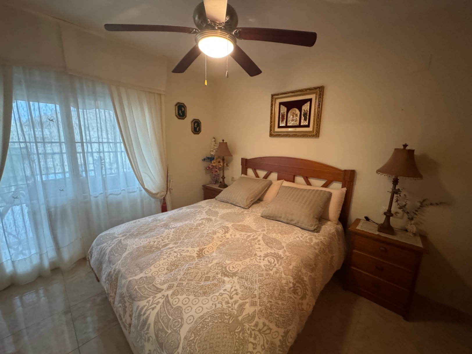 Habitación con cama de madera, ropa de cama estampada y ventilador de techo con luz.