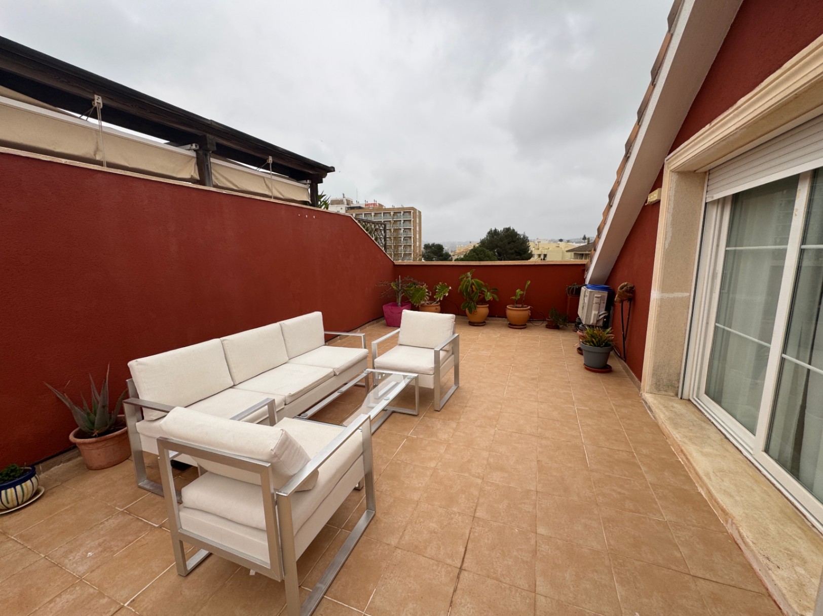Terraza con suelo cerámico, paredes rojas y muebles de exterior de aluminio.