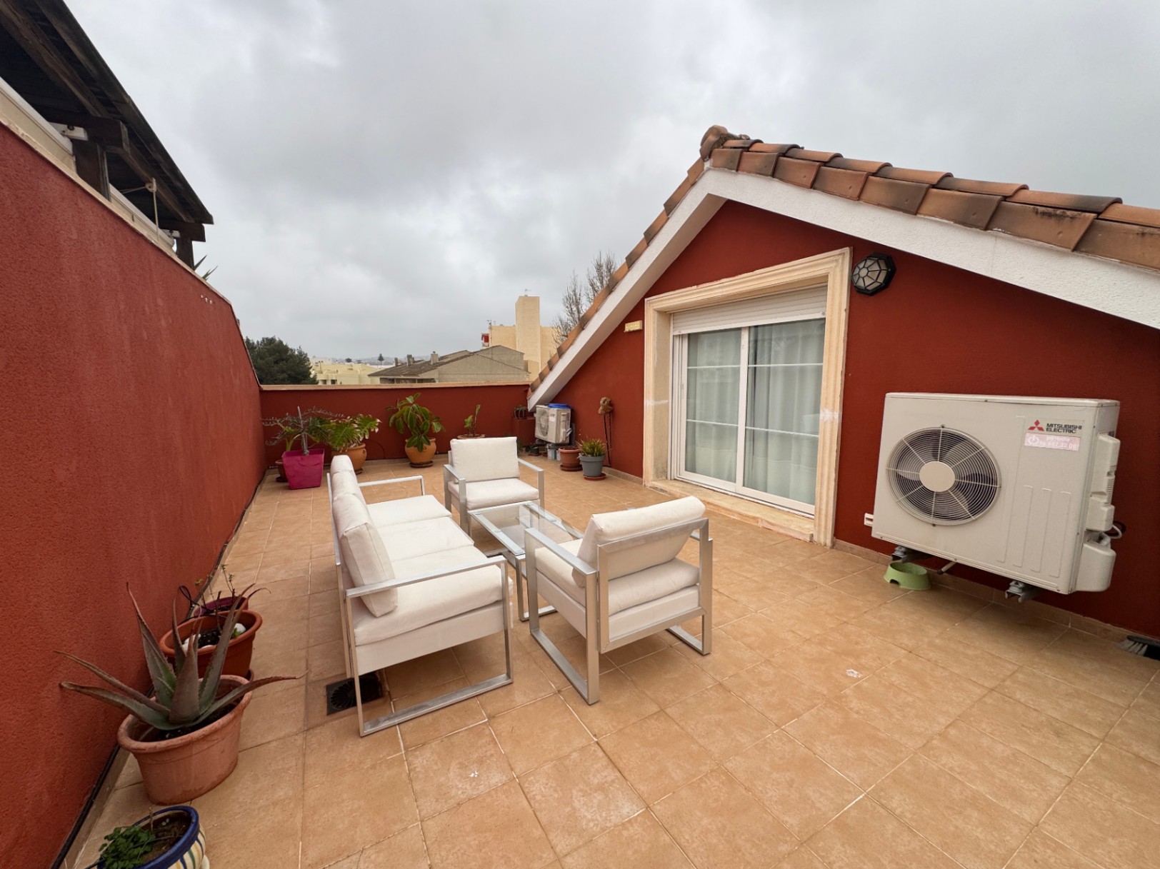 Terraza con suelo de baldosas, paredes rojas y muebles de exterior blancos.