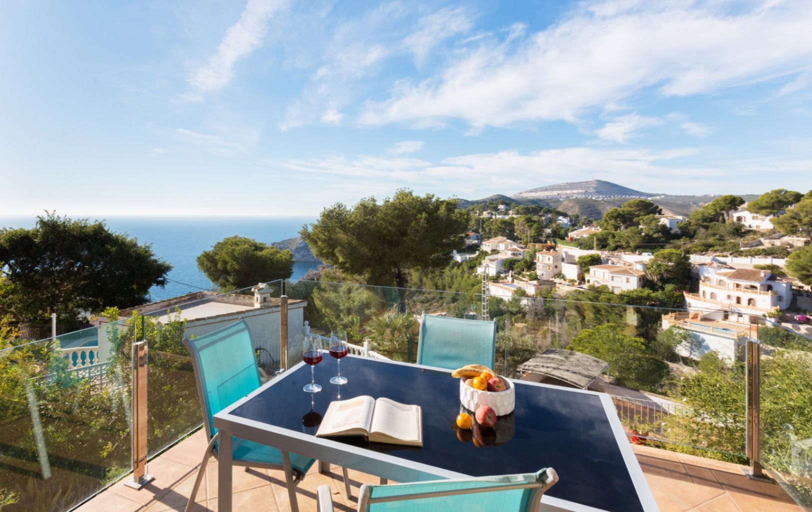Terraza con barandilla de cristal, mesa de comedor de cristal negro y vistas panorámicas a la costa mediterránea y las colinas de Cumbre del Sol.