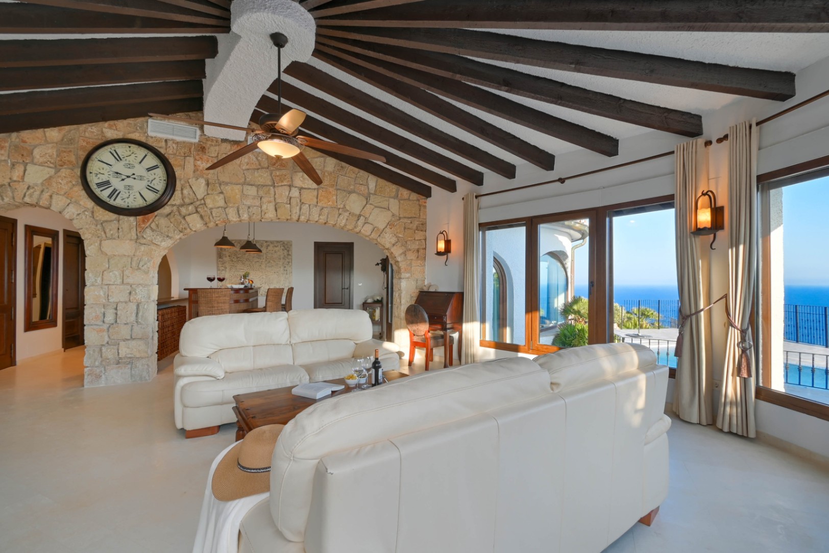 Salón con techo abovedado de vigas de madera radiales, arco de piedra natural y amplios ventanales con vistas panorámicas al mar Mediterráneo.