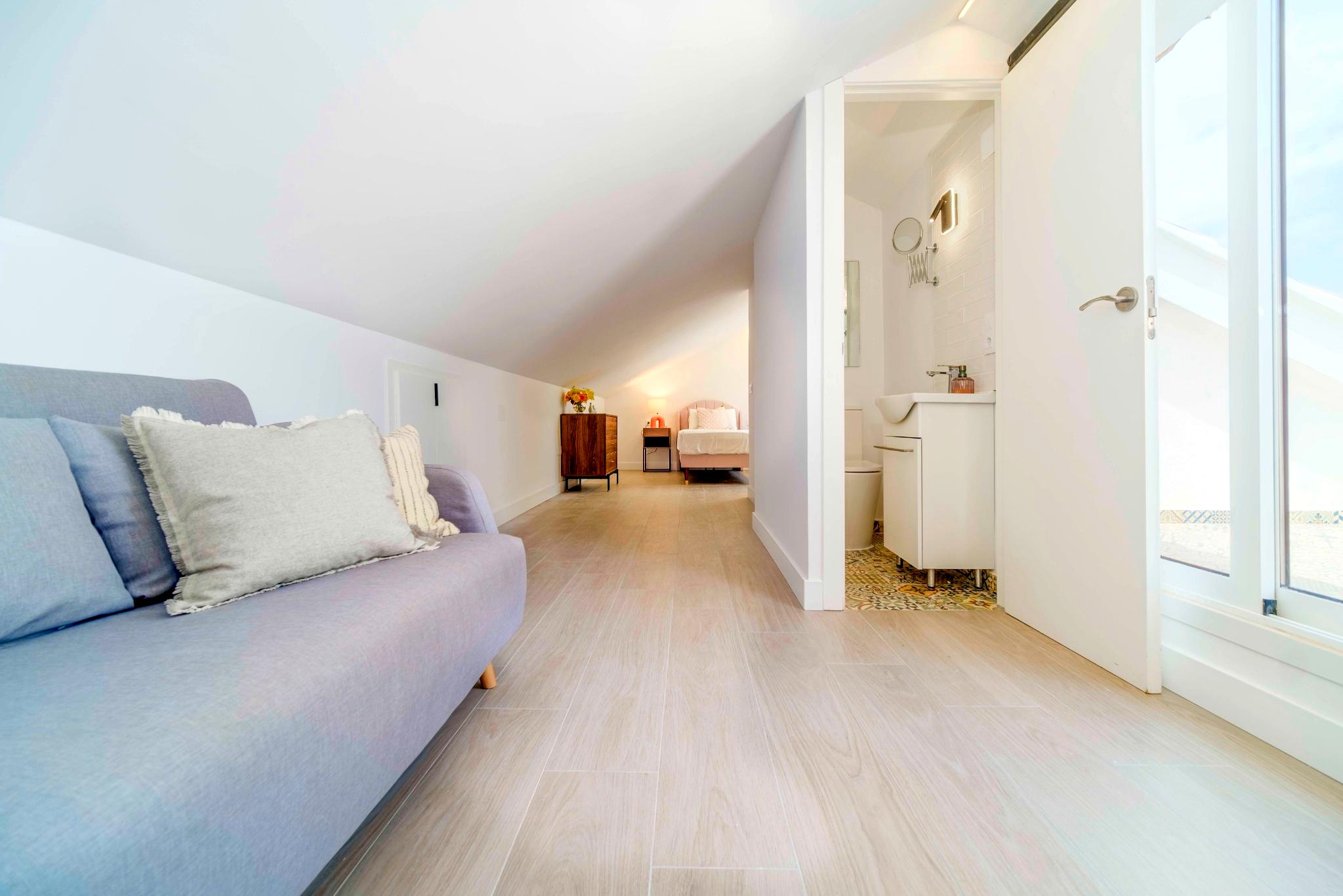 Suite abuhardillada con techos inclinados, suelos de gres efecto madera, zona de estar y baño integrado con azulejos de diseño hidráulico.