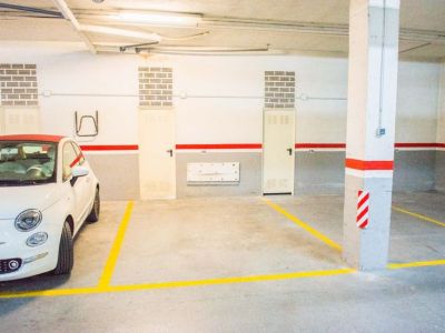 Amplia plaza de aparcamiento subterráneo con claras marcas amarillas en suelo de hormigón. Incluye iluminación cenital, pilares y trasteros individuales.