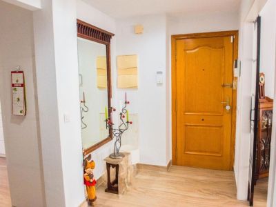 El recibidor presenta una puerta principal de madera clara, suelo de gres porcelánico y un gran espejo con marco decorado. A la izquierda se vislumbra la cocina moderna.
