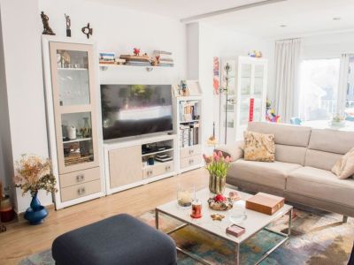 Luminoso salón con sofá beige, mesa de centro moderna con tapa de mármol y mueble de TV blanco. La luz natural entra por amplias puertas de cristal hacia una terraza.