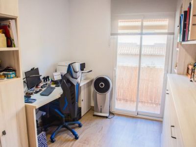 Oficina en casa funcional con suelo laminado de madera clara y luz natural de una puerta corredera de cristal. Incluye escritorio, silla ergonómica y estanterías integradas para almacenamiento.
