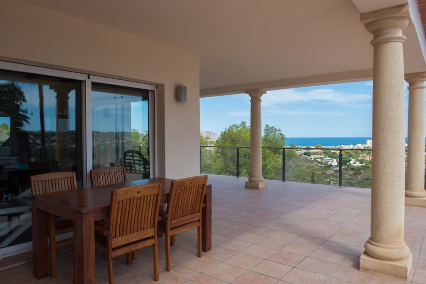Amplia terraza cubierta con comedor de madera, suelo de baldosas y columnas de piedra clásicas. Disfrute de vistas panorámicas al mar y la ciudad a través de la barandilla de cristal, accesible por puertas correderas. Amplia terraza cubierta con comedor de madera, suelo de baldosas y columnas de piedra clásicas. Disfrute de vistas panorámicas al mar y la ciudad a través de la barandilla de cristal, accesible por puertas correderas.