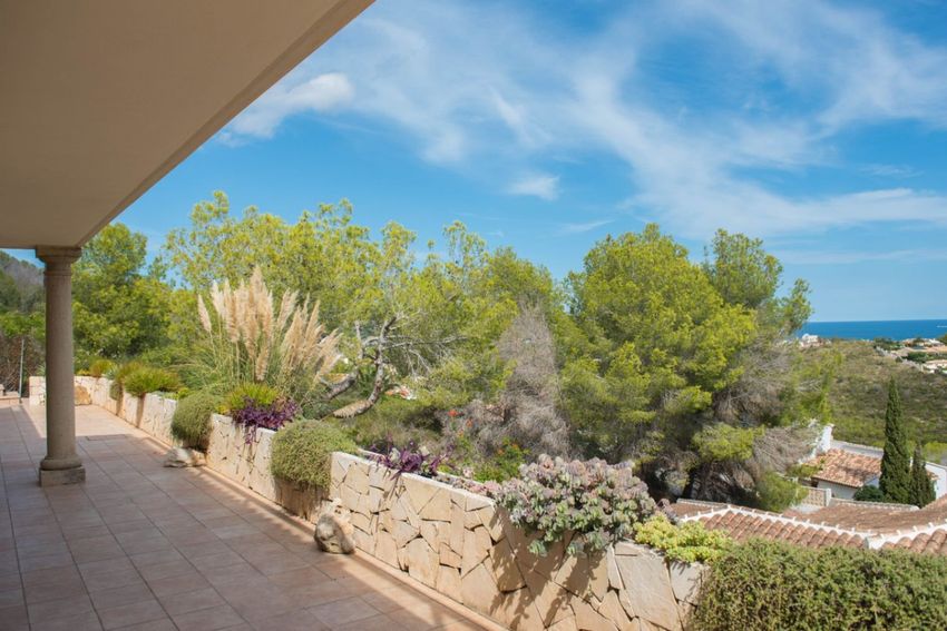 Amplia terraza exterior con suelo de baldosas y muro de piedra natural, adornada con pampas y vegetación mediterránea, ofreciendo vistas parciales al mar y tejados. Amplia terraza exterior con suelo de baldosas y muro de piedra natural, adornada con pampas y vegetación mediterránea, ofreciendo vistas parciales al mar y tejados.