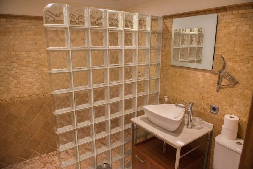 Baño con distintiva pared de pavés, azulejos de mosaico en tonos tierra y un moderno lavabo triangular sobre encimera de mármol. Baño con distintiva pared de pavés, azulejos de mosaico en tonos tierra y un moderno lavabo triangular sobre encimera de mármol.