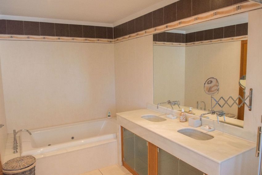 Baño principal con doble lavabo de mármol, espejo grande y bañera empotrada. Las paredes combinan azulejos claros con un friso decorativo marrón. Baño principal con doble lavabo de mármol, espejo grande y bañera empotrada. Las paredes combinan azulejos claros con un friso decorativo marrón.