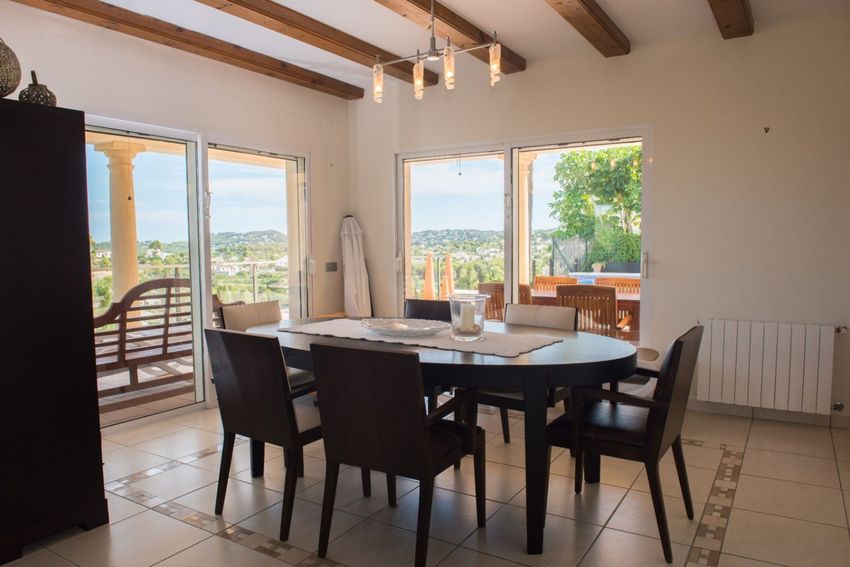 Comedor con mesa ovalada de madera oscura, techo con vigas vistas y suelo de gres. Grandes puertas correderas ofrecen vistas panorámicas y acceso a la terraza. Comedor con mesa ovalada de madera oscura, techo con vigas vistas y suelo de gres. Grandes puertas correderas ofrecen vistas panorámicas y acceso a la terraza.