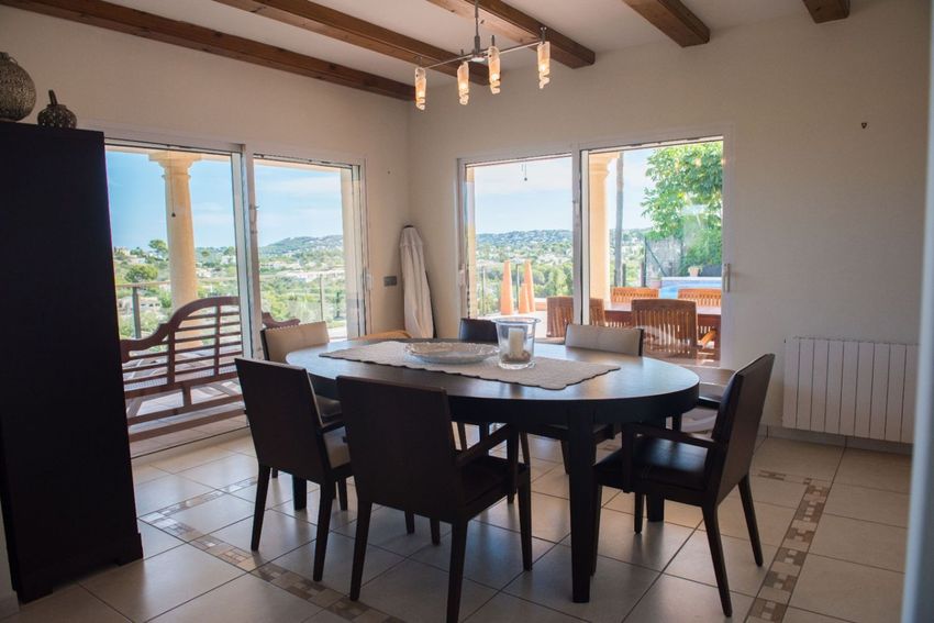 Comedor con mesa ovalada y sillas de cuero, ofreciendo vistas panorámicas a las colinas a través de amplios ventanales. Techo con vigas de madera y suelo de baldosas. Comedor con mesa ovalada y sillas de cuero, ofreciendo vistas panorámicas a las colinas a través de amplios ventanales. Techo con vigas de madera y suelo de baldosas.