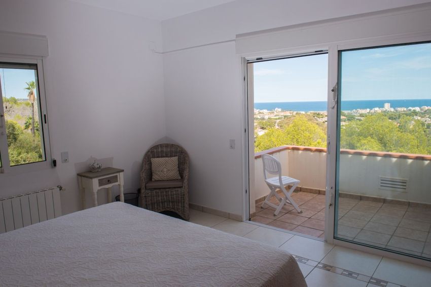 Dormitorio con acceso directo a balcón privado, ofreciendo vistas panorámicas al mar y la costa. Incluye suelo de baldosas y silla de mimbre. Dormitorio con acceso directo a balcón privado, ofreciendo vistas panorámicas al mar y la costa. Incluye suelo de baldosas y silla de mimbre.