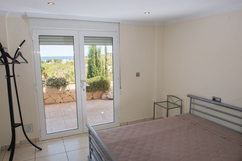 Dormitorio con cama de estructura metálica, suelo de baldosas y acceso directo a una terraza exterior con vistas lejanas al mar Mediterráneo. Dormitorio con cama de estructura metálica, suelo de baldosas y acceso directo a una terraza exterior con vistas lejanas al mar Mediterráneo.