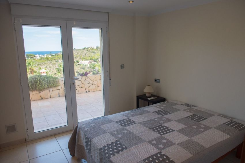 Dormitorio con cama de patchwork y acceso directo a una terraza exterior, ofreciendo vistas panorámicas al mar Mediterráneo y al paisaje de Jávea. Dormitorio con cama de patchwork y acceso directo a una terraza exterior, ofreciendo vistas panorámicas al mar Mediterráneo y al paisaje de Jávea.