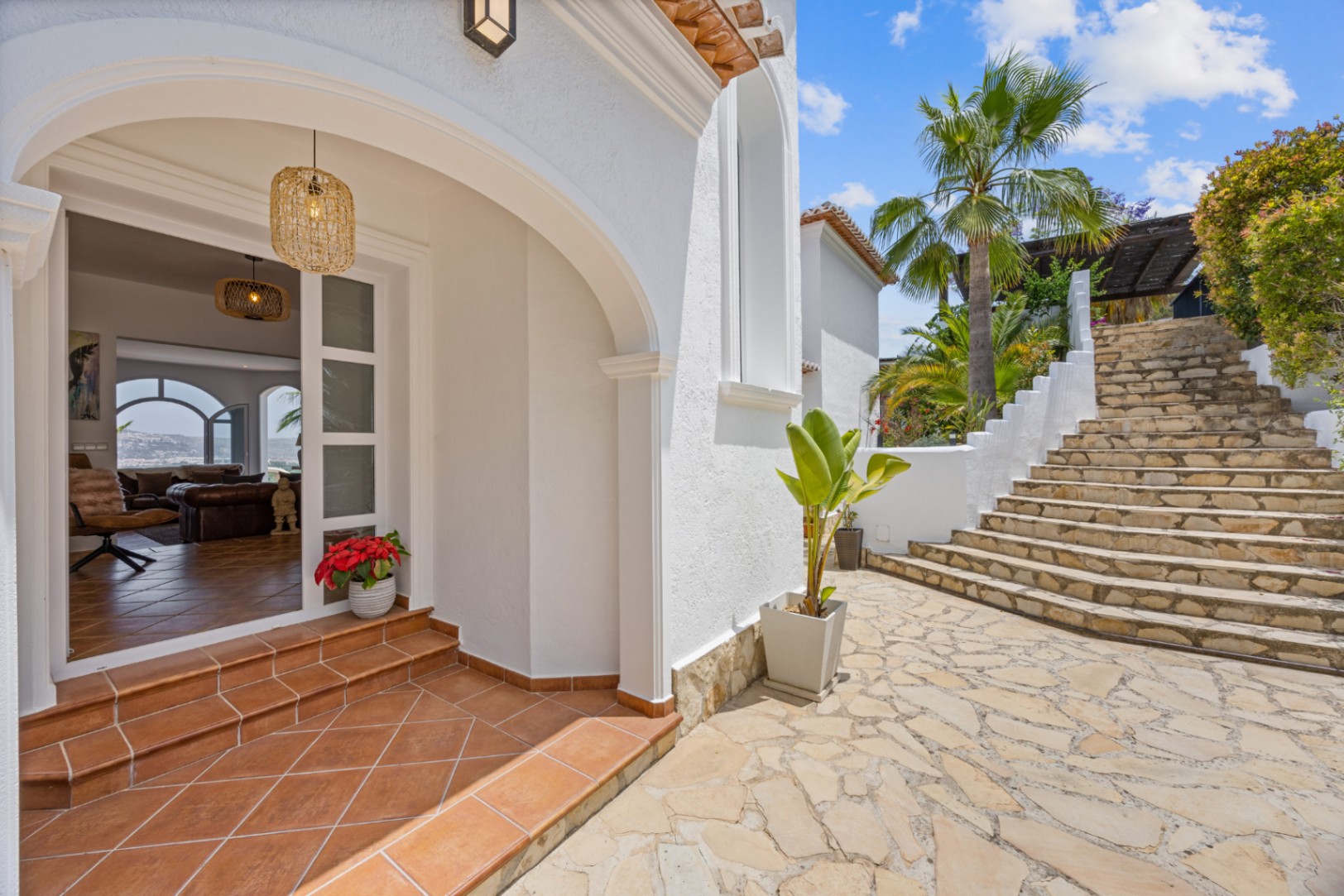 Entrada con arco blanco, peldaños de terracota y pavimento de piedra natural que conduce a una escalera exterior rodeada de vegetación mediterránea.