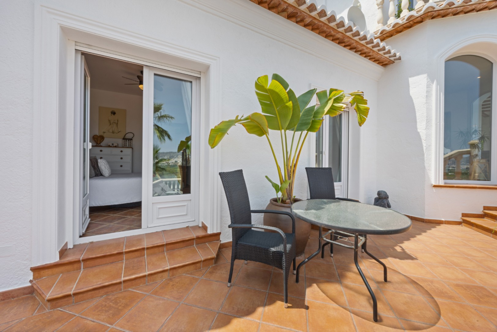 Terraza con suelos de terracota, mobiliario de exterior y acceso directo a un dormitorio luminoso a través de puertas correderas acristaladas.