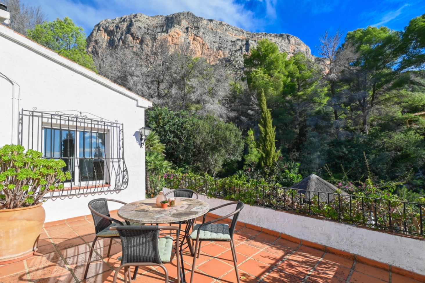 Terraza con suelos de terracota y mobiliario de piedra, con vistas directas al bosque y al macizo montañoso bajo un cielo despejado.