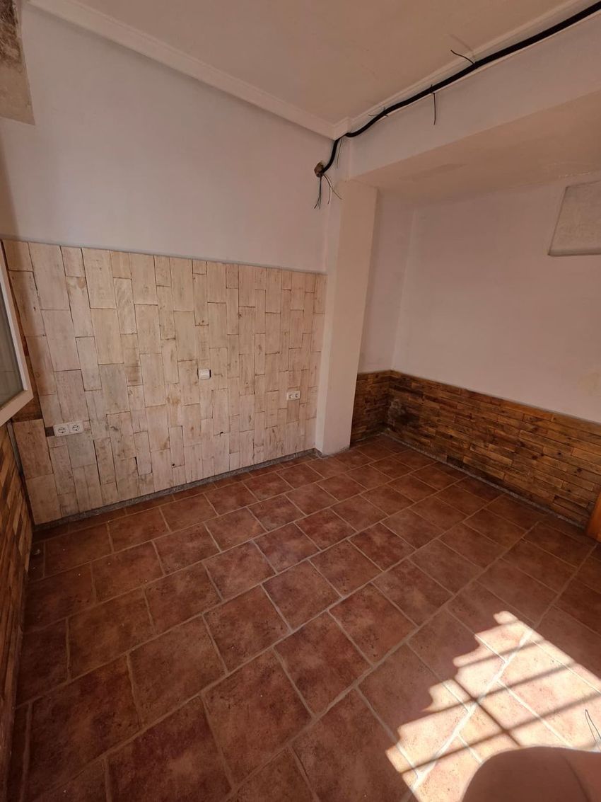 Espacio interior con suelo de baldosas de terracota y paredes parcialmente revestidas con dos tipos de panelado de madera. La luz natural crea sombras en el suelo, mostrando un ambiente en fase de actualización. Espacio interior con suelo de baldosas de terracota y paredes parcialmente revestidas con dos tipos de panelado de madera. La luz natural crea sombras en el suelo, mostrando un ambiente en fase de actualización.