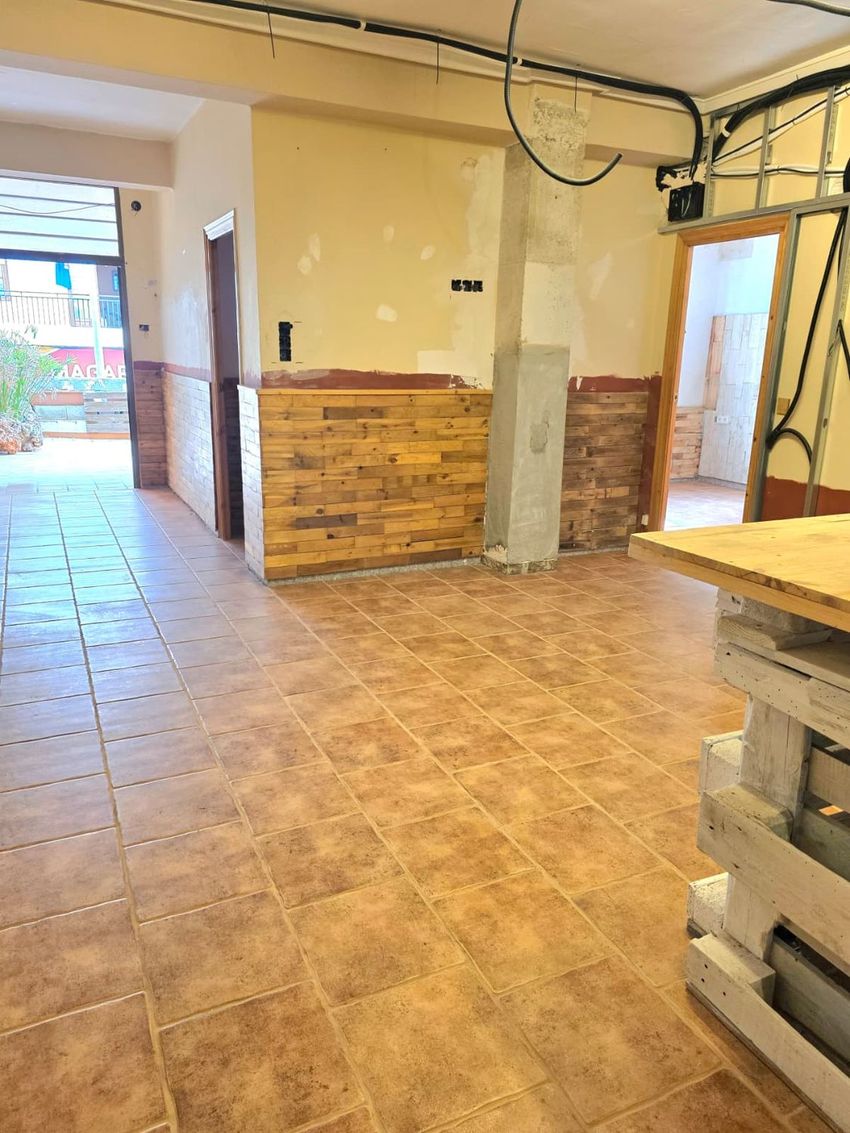 Espacio interior en fase de actualización, con suelo de baldosas terracota, revestimiento parcial de madera y cableado eléctrico expuesto. Un pilar de hormigón y un mostrador de palets son visibles, ofreciendo personalización. Espacio interior en fase de actualización, con suelo de baldosas terracota, revestimiento parcial de madera y cableado eléctrico expuesto. Un pilar de hormigón y un mostrador de palets son visibles, ofreciendo personalización.
