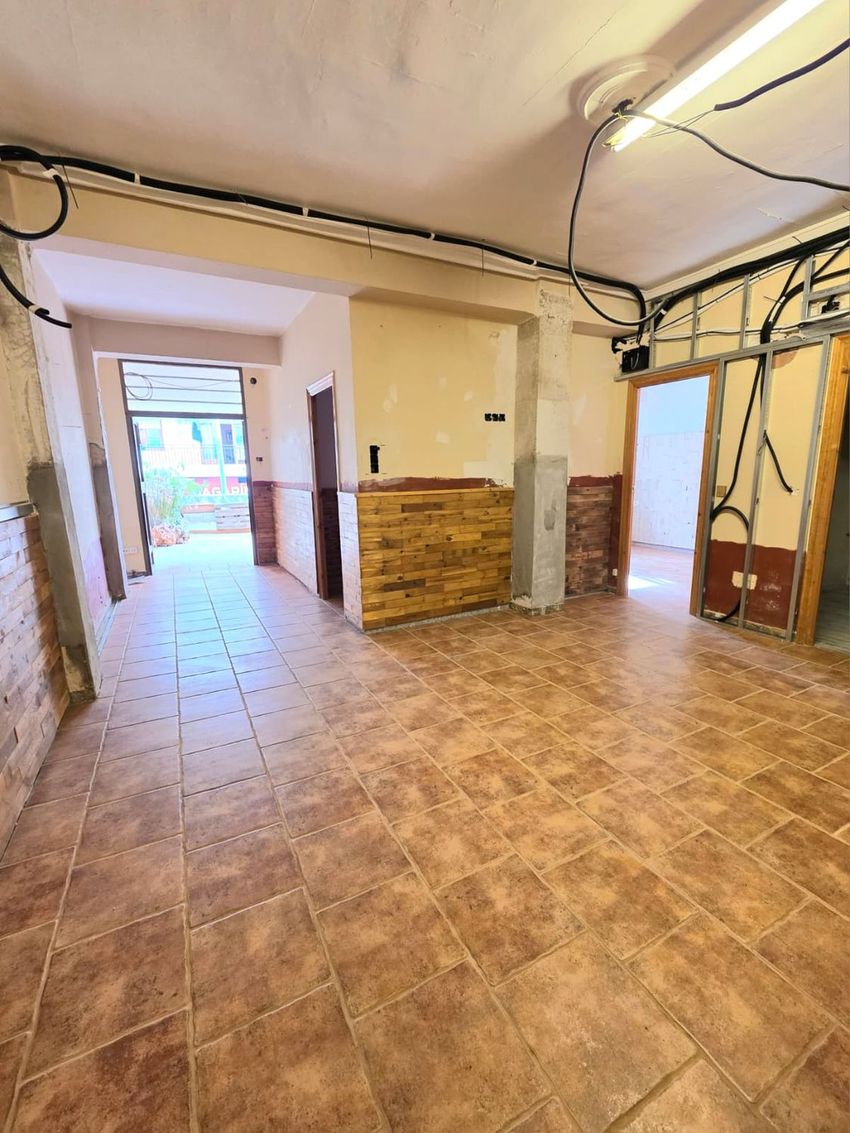 Espacio interior en fase de actualización con suelo de baldosas terracota. Se aprecian paredes con revestimiento parcial de madera y ladrillo visto, y una salida a patio exterior. Espacio interior en fase de actualización con suelo de baldosas terracota. Se aprecian paredes con revestimiento parcial de madera y ladrillo visto, y una salida a patio exterior.