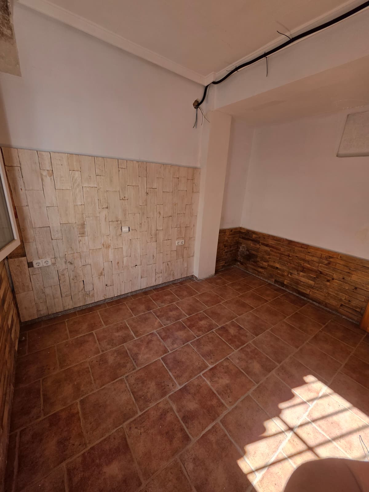 Habitación interior con suelo de baldosas de terracota y pared decorativa de listones de madera clara. Incluye cableado visto y varias tomas de corriente.