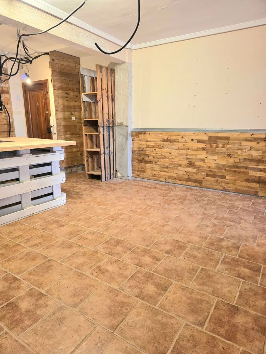 Suelo de baldosas terracota. Paredes con paneles de madera rústica y zona pintada. Mostrador de palets y estantería de madera, con cableado expuesto en el techo. Suelo de baldosas terracota. Paredes con paneles de madera rústica y zona pintada. Mostrador de palets y estantería de madera, con cableado expuesto en el techo.