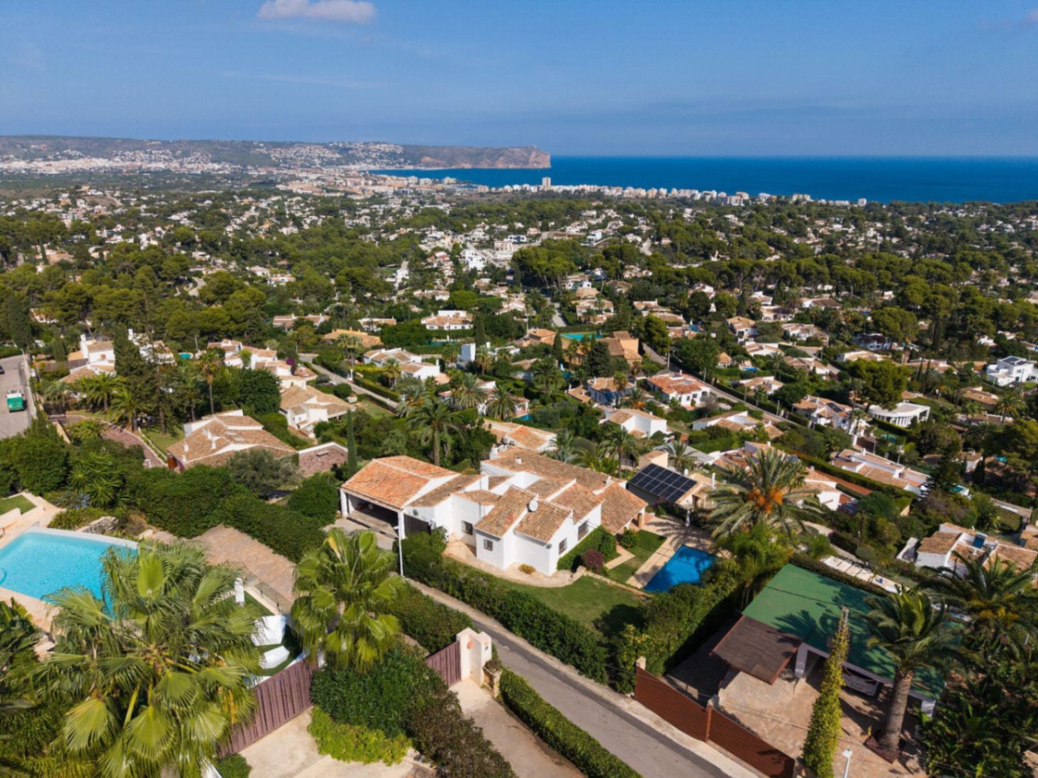 Vista aérea de una urbanización costera con villas blancas de tejados cerámicos, piscinas privadas y amplias vistas panorámicas hacia el mar Mediterráneo.