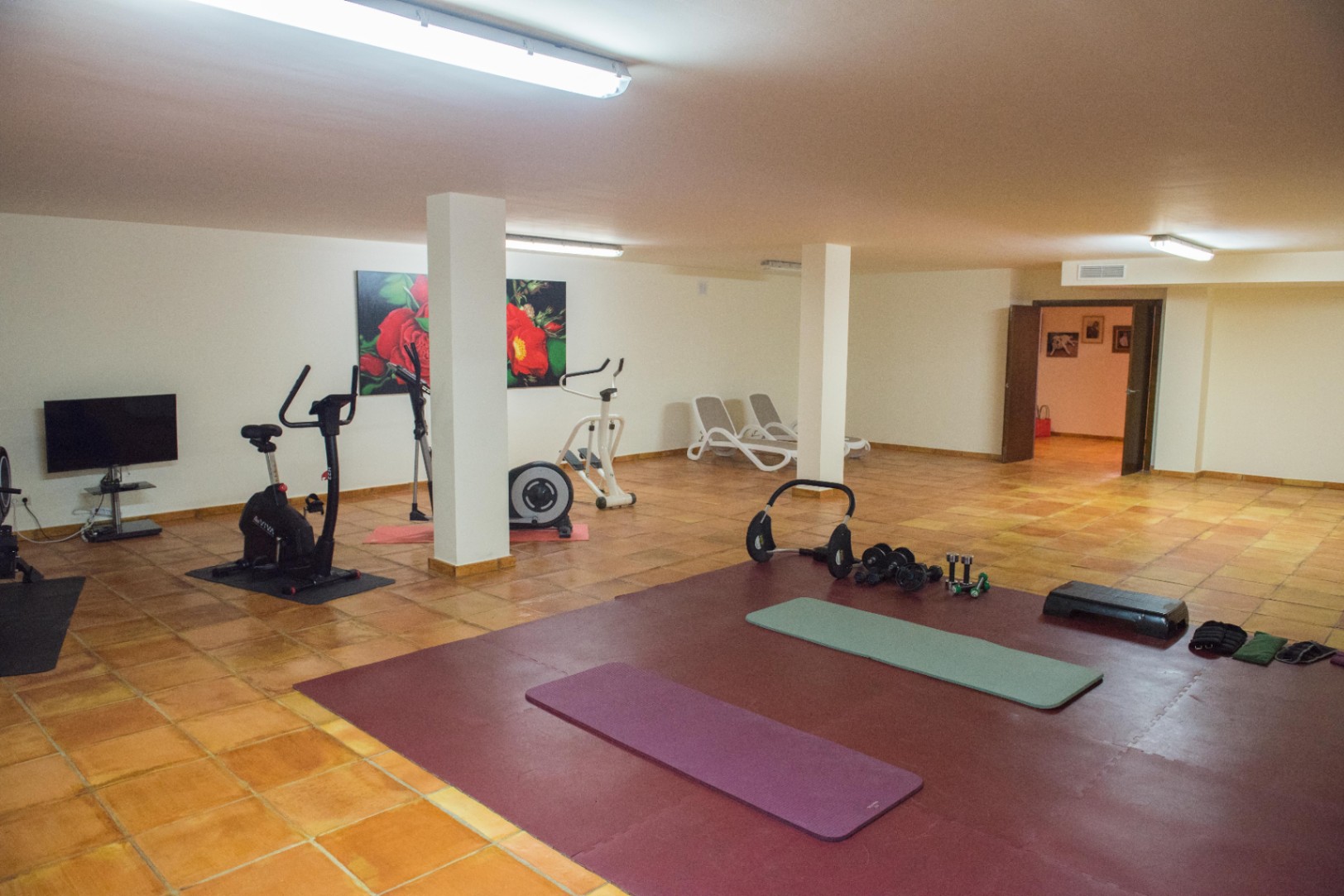 Gimnasio con suelo de terracota, equipamiento variado y luz fluorescente.