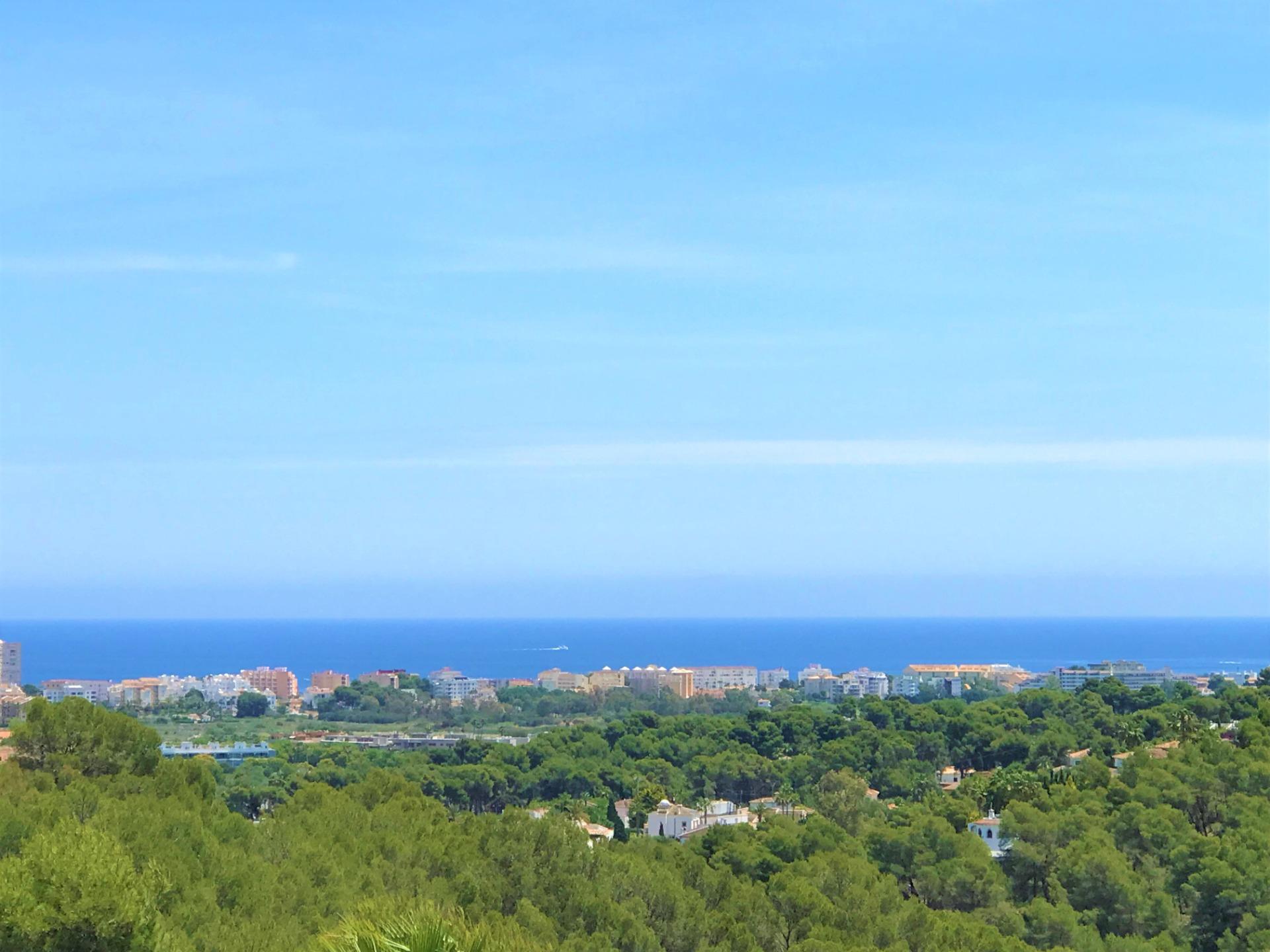 Vista panorámica del litoral mediterráneo con un denso pinar en primer plano y arquitectura costera bajo un horizonte despejado y azul.