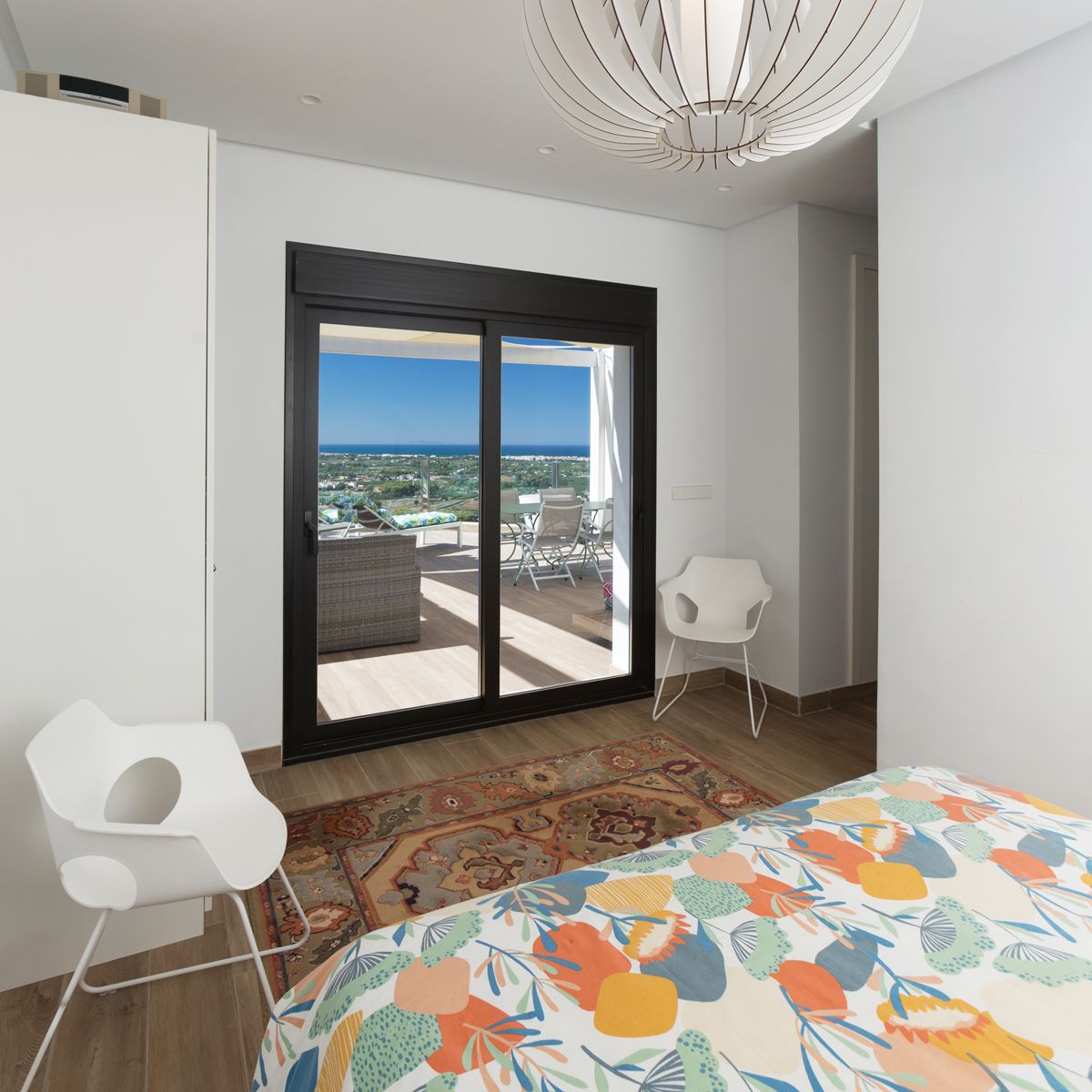 Dormitorio con edredón colorido, suelo de madera y acceso directo a una terraza privada. Grandes puertas correderas enmarcan vistas panorámicas al mar y la costa, maximizando la luz natural. Dormitorio con edredón colorido, suelo de madera y acceso directo a una terraza privada. Grandes puertas correderas enmarcan vistas panorámicas al mar y la costa, maximizando la luz natural.