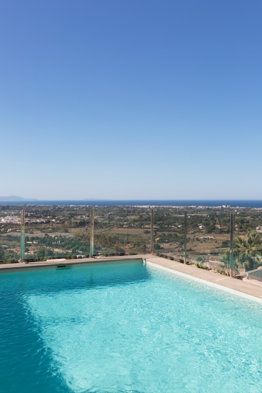 Piscina de borde infinito con agua azul cristalina y barandilla de cristal, ofreciendo vistas panorámicas al paisaje costero y al mar Mediterráneo bajo un cielo despejado. Piscina de borde infinito con agua azul cristalina y barandilla de cristal, ofreciendo vistas panorámicas al paisaje costero y al mar Mediterráneo bajo un cielo despejado.