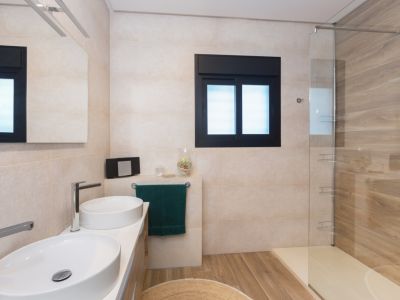 Baño moderno con doble lavabo ovalado, grifería cromada y espejo iluminado. Ducha de obra con mampara de cristal, pared de azulejos efecto madera y suelo de gres porcelánico a juego.
